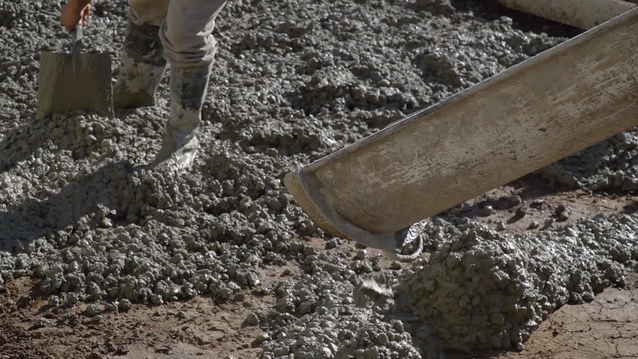 Slow-motion close-up of a worker laying fresh asphalt on a street using a shovel.
