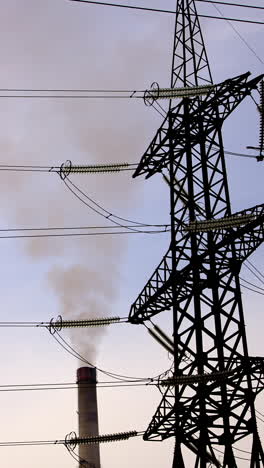 dirty smoke from pipe near transmission lines.high voltage power line support and smoke from the chimney of the industrial plant. ecology and environmental pollution. vertical video