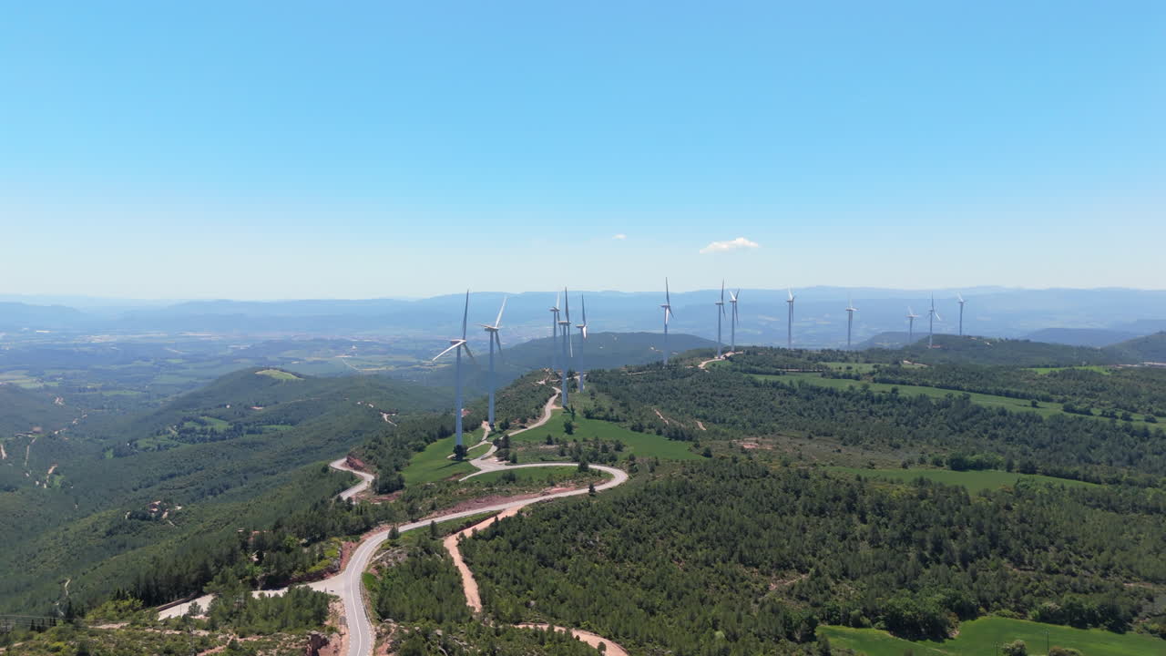 Drone performs a smooth orbit around multiple wind turbines over a green mountainous landscape on a sunny day. Renewable energy, clean technology and natural terrain combined in cinematic motion