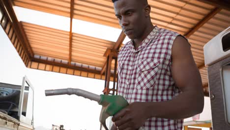 hombre afroamericano en camisa sin mangas usando bomba de combustible en la gasolinera