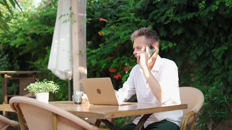 businessman drinking beverage and talking on cellphone in street restaurant