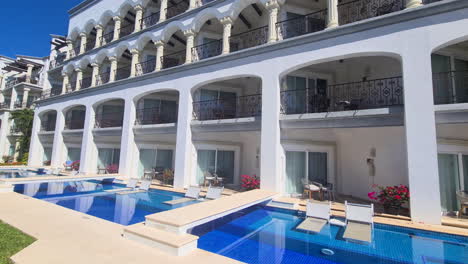 luxury tropical resort building, private swimming pools and white facade on hot sunny day