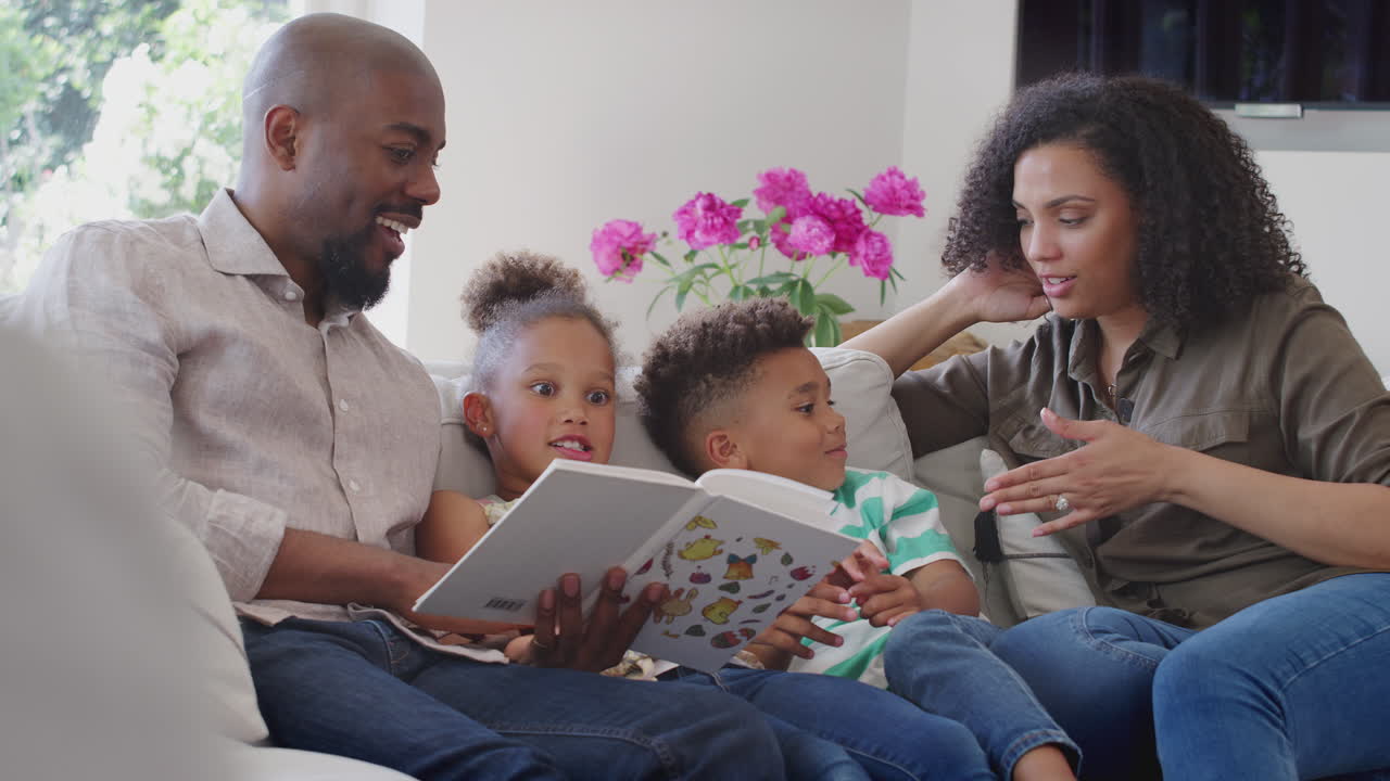 Genitori seduti sul divano a casa con i figli che leggono un libro insieme.