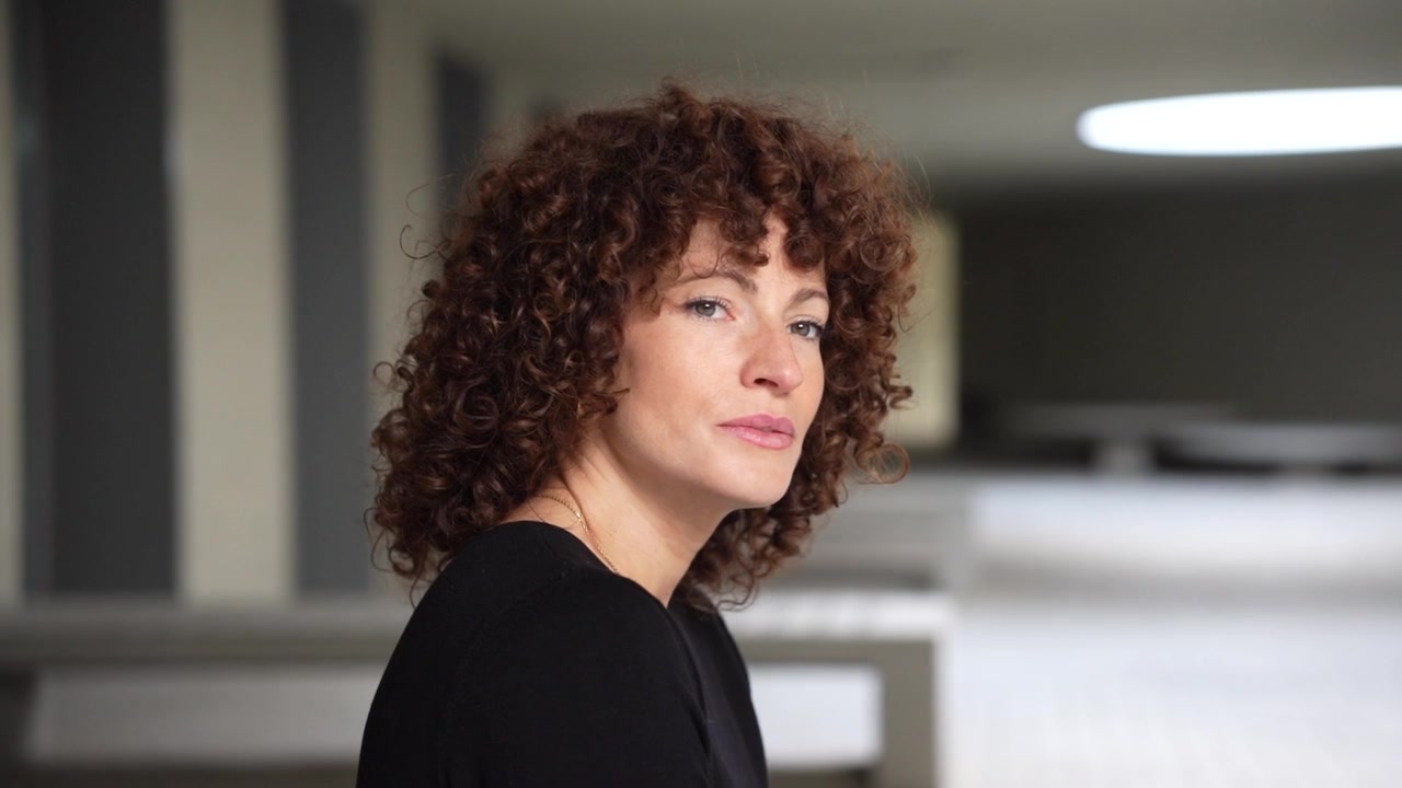 Una donna pensierosa con i capelli ricci, ritratta in un bellissimo spazio moderno che emana eleganza.