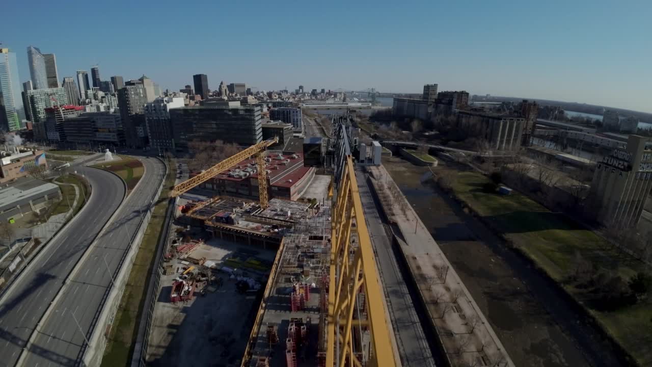 una grúa amarilla se eleva sobre un sitio de construcción con el horizonte en el viejo puerto, montreal, canadá - toma de fpv
