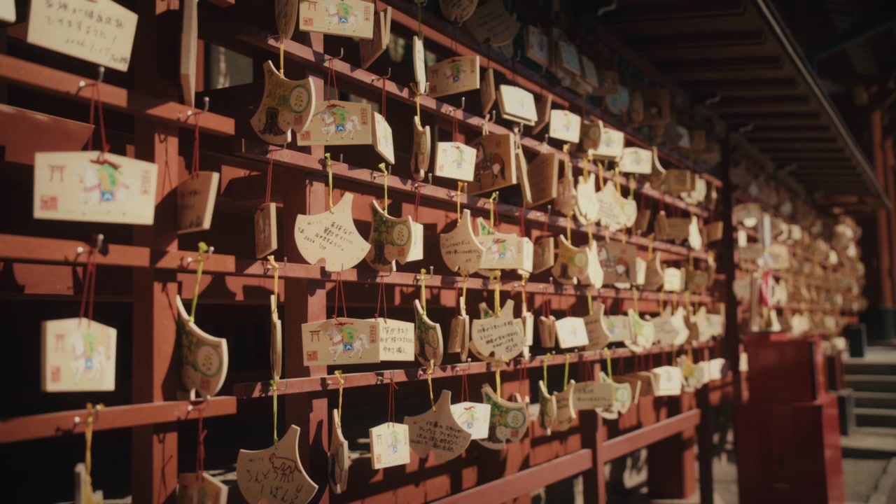 Numerose placche ema in legno appese in file ordinate al Tsurugaoka Hachiman-gu, il più importante santuario shintoista di Kamakura, ognuna incisa con preghiere scritte a mano, con la calda luce del sole che proietta lunghe ombre