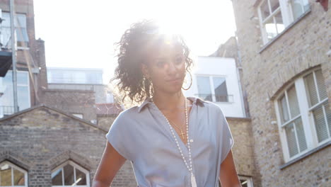 Fashionable-young-black-woman-in-blue-dress-standing-in-sunlight-on-the-street,-backlit,-low-angle