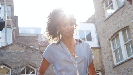 joven negra de moda en vestido azul de pie a la luz del sol en la calle, retroiluminada, ángulo bajo