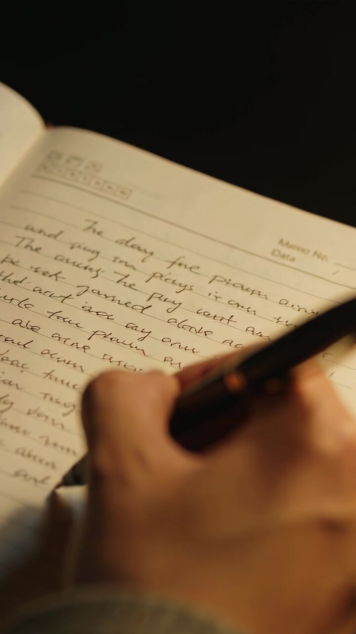 Vertical video: Writing hand with gray cuff holding pen entering page writing cursive notes at desk