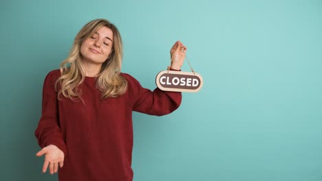 Young woman showing closed sign in blue studio
