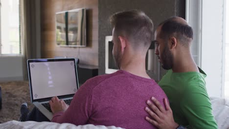 pareja de hombres homosexuales multiétnicos sentados en el sofá mirando juntos la computadora portátil