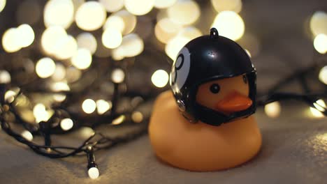fotografía en primer plano de un pato de goma con un casco de motocicleta hecho a mano sobre el fondo de una guirnalda de navidad