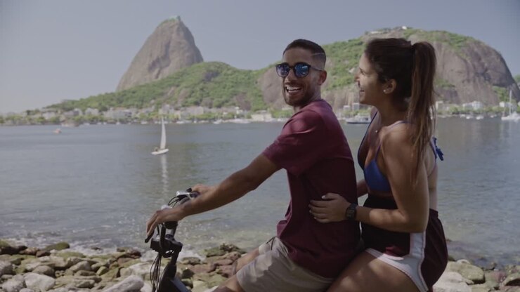 Smiling couple cycling along the waterfront in Rio de Janeiro with Sugarloaf Mountain in the background