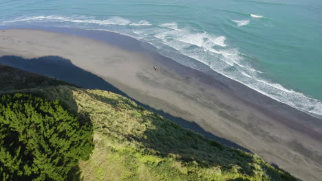 a couple rise horseback raglan beach in new zealand along hillside