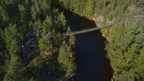 Floating-bridge-on-ropes-over-a-lake-or-a-stream-in-a-forest,-summer,-aerial-revealing-shot