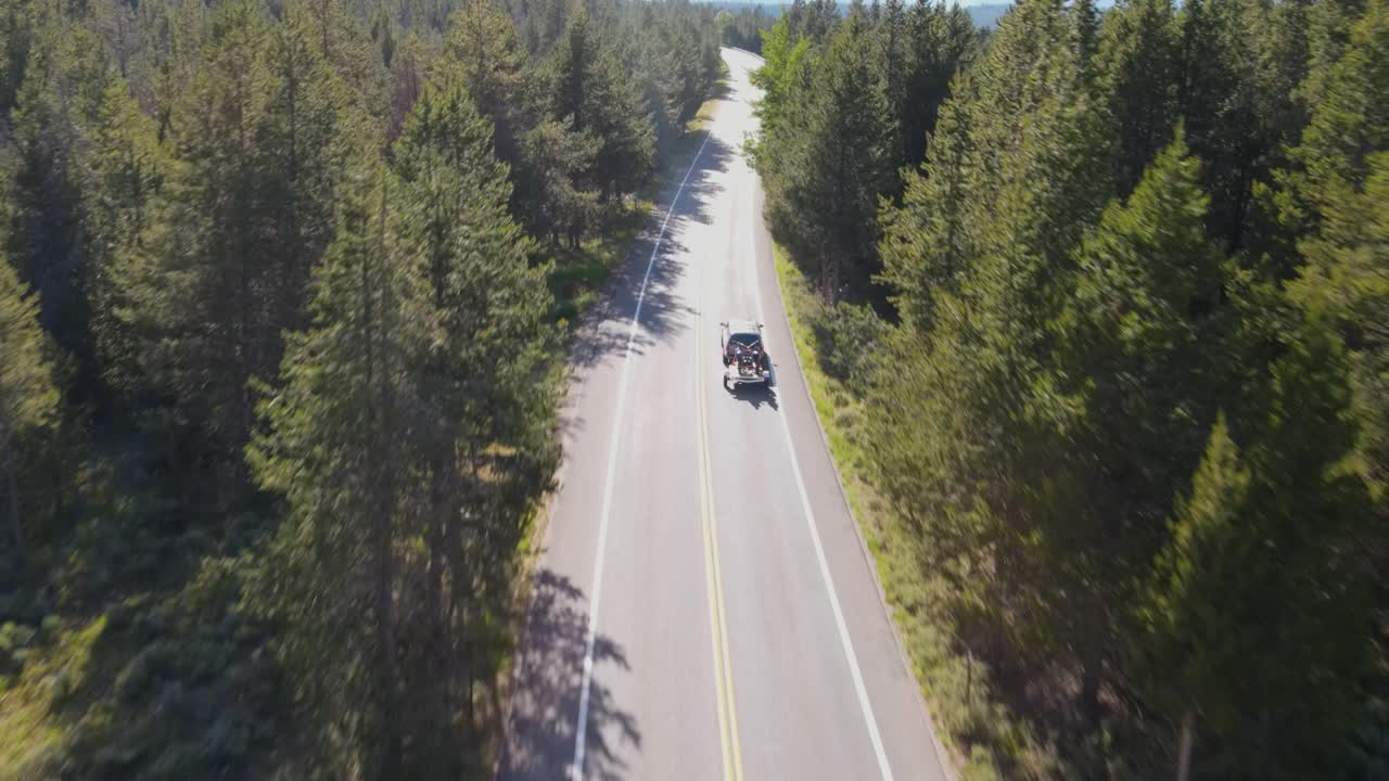 A 4K drone shot of a truck driving on a remote road surrounded by forest