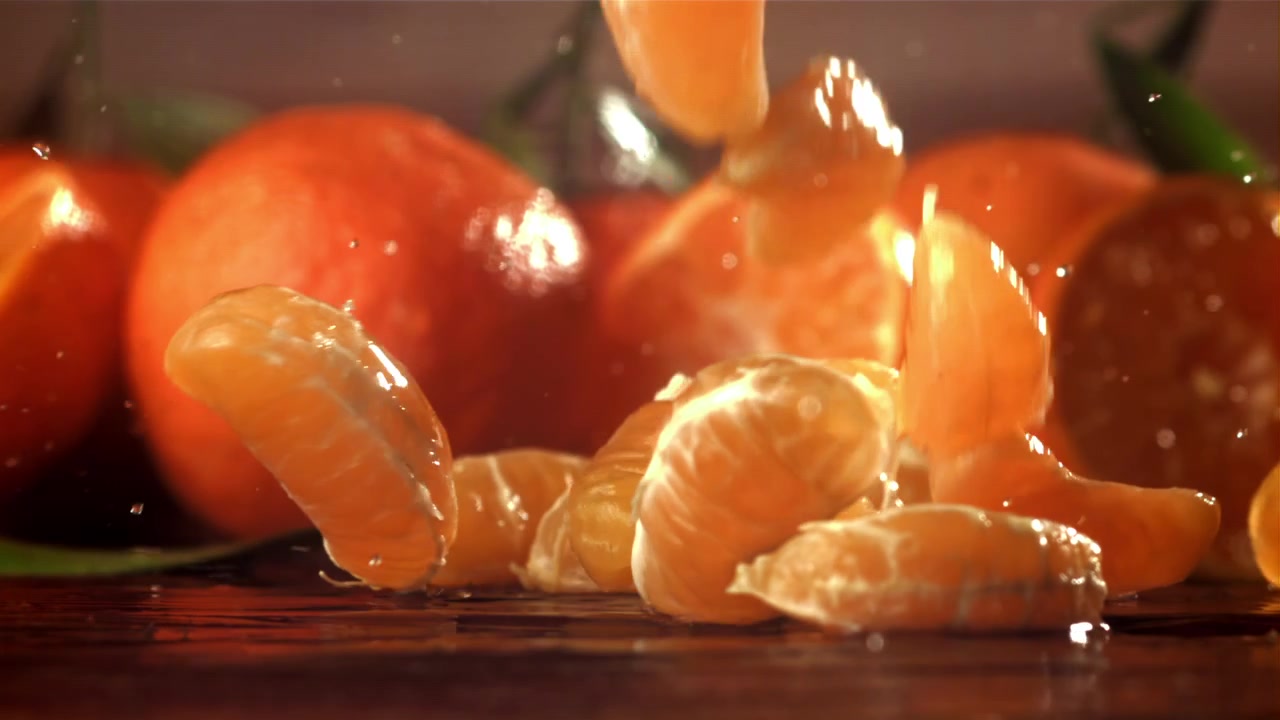 Mandarinskiver faller og spruter på våt overflate i sakte film