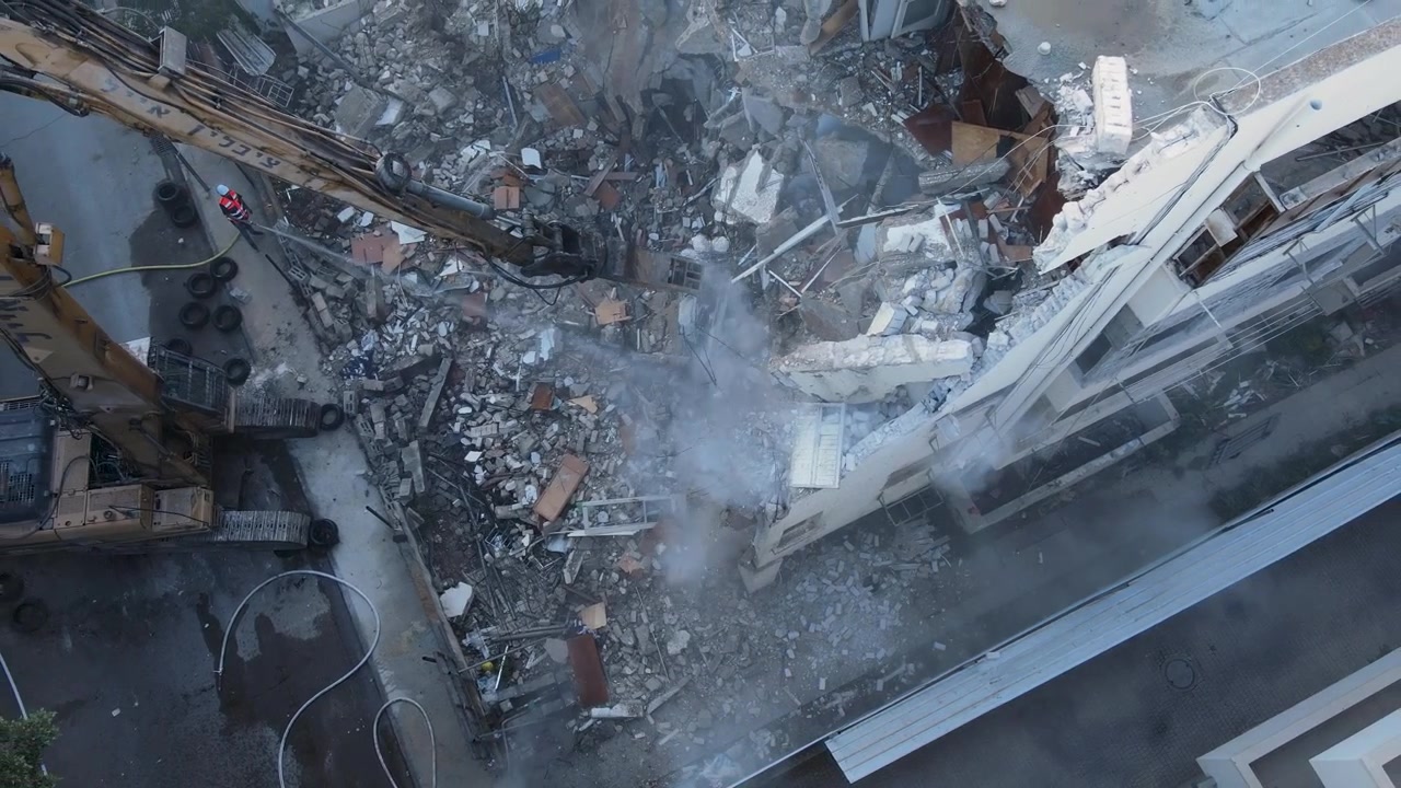 Primo piano aereo dall'alto di una gru che afferra un pezzo di muro in un cantiere di demolizione durante operazioni di riqualificazione urbana, ripreso da drone.