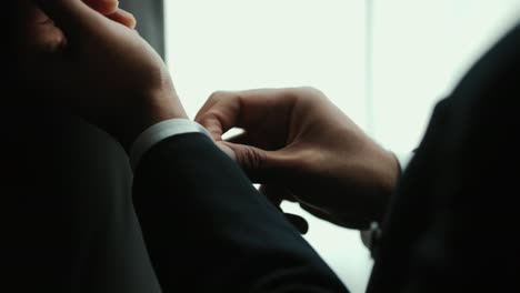 confident businessman in classic blue suit buttoning or adjust cufflinks near window in hotel room at the morning. handsome man wearing a nice suit on wedding day.