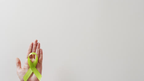 video of hand holding pale green std awareness ribbon on white background with copy space