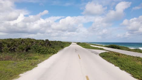 tiro de ángulo bajo de una mujer joven conduciendo un scooter rojo por una carretera a lo largo del océano ubicado en la isla tropical de cozumel, méxico filmada en 4k