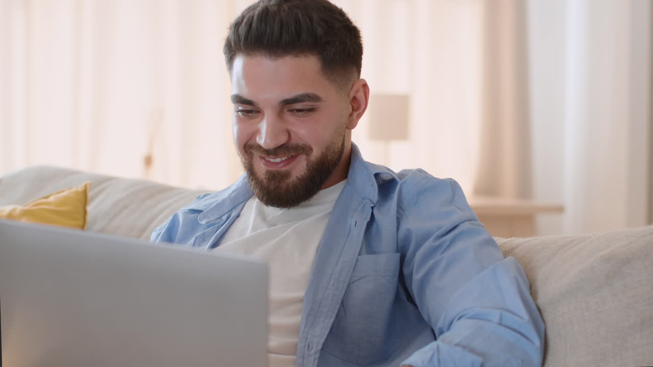 Smiling man working on laptop from his couch at home