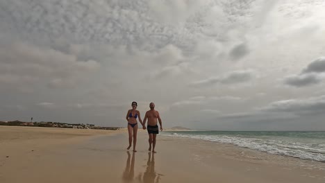 romantic couple walks hand in hand along peaceful, sandy beach of boa vista island with cloudy sky overhead, creating serene and intimate moment by the ocean, cape verde. slow motion
