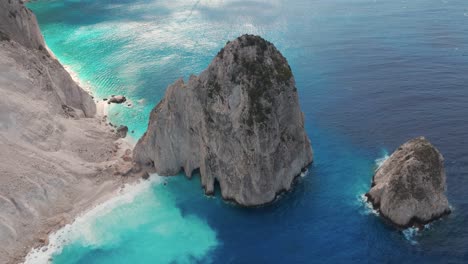 Drohnenaufnahme-Von-Felsen-Im-Blauen-Meer-Und-Einsamer-Weißer-Sandstrand-Unter-Klippen-Der-Insel-Zakynthos,-Griechenland-50fps