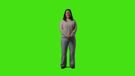 full length shot of smiling casually dressed young woman standing against green screen with hands in pockets