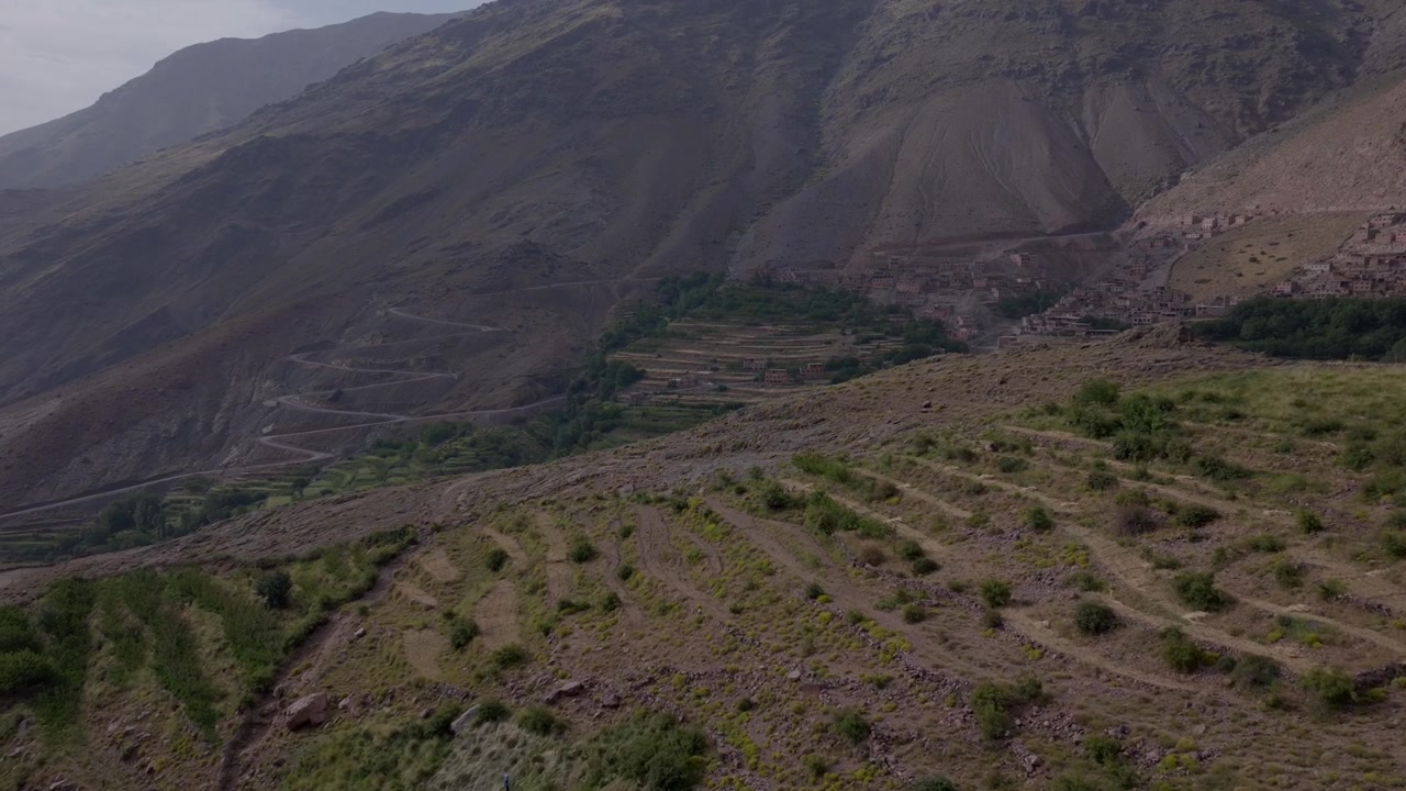 Veduta aerea di estese terrazze agricole collinari e tortuose strade a tornanti che si snodano tra i pendii delle montagne dell'Alto Atlante in Marocco
