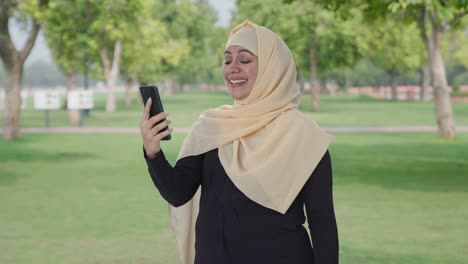 happy muslim woman talking on video call in park