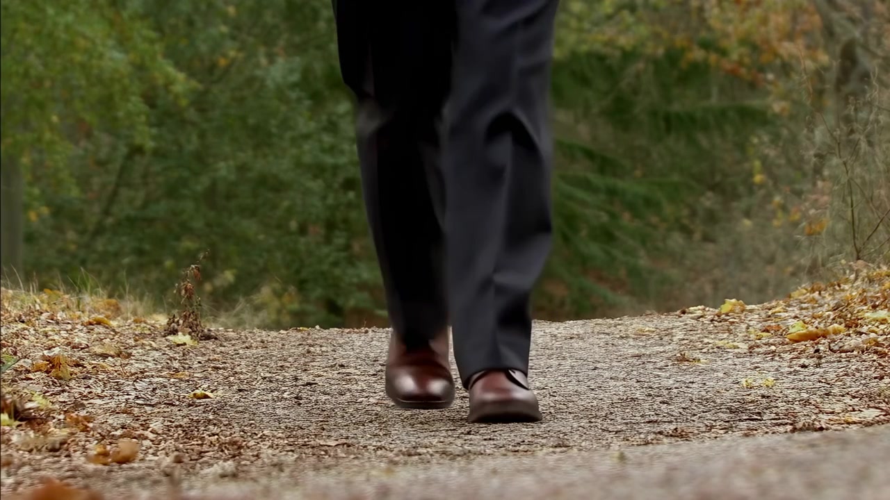 Primo piano di scarpe che camminano su un sentiero di ghiaia, un professionista in abito cammina con passo deciso lungo un sentiero forestale autunnale, scarpe di pelle