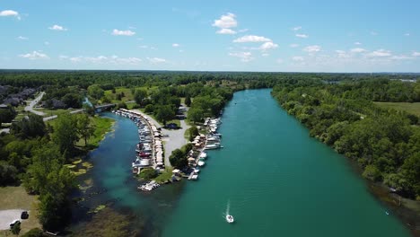 ascending aerial backwards shot of niagara river with luxury boats at pier,driving cars on street and green forest landscape in canada