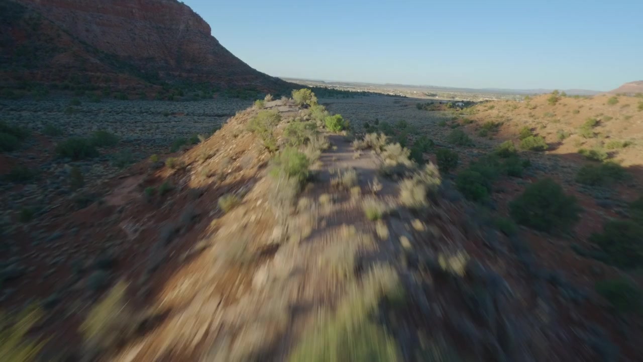 Volo FPV veloce sopra un aspro canyon desertico dell'Arizona con terreno rosso e vegetazione arbustiva