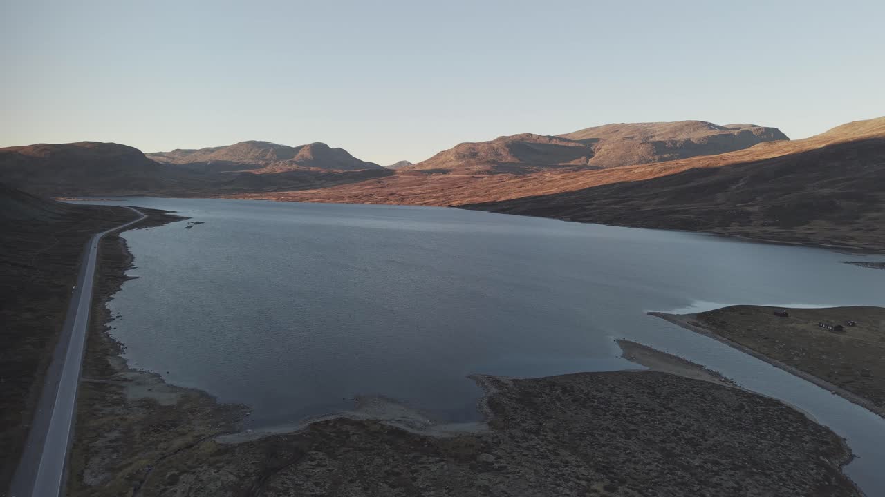 A road along mountain lake and surrounding mountains at sunset in Norway. Drone footage