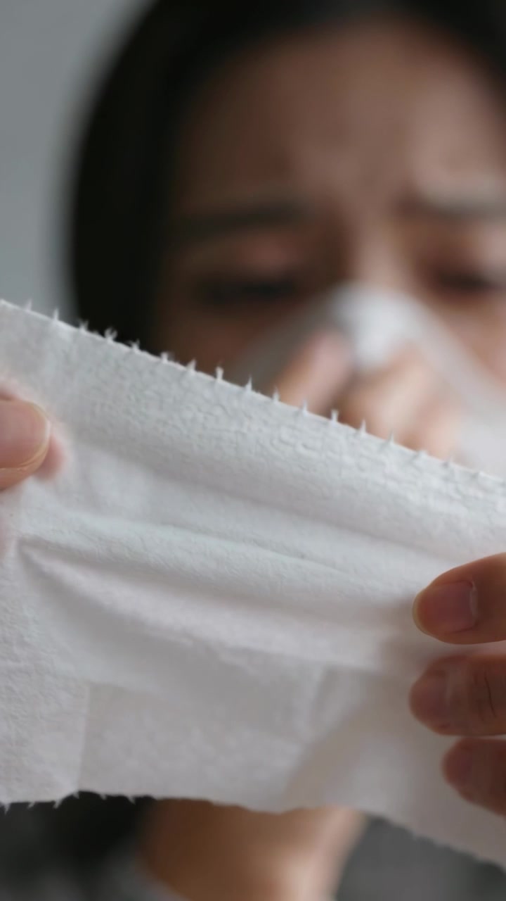 Vertical video: Holding torn tissue, adult woman pressing it to nose near wall, sneeze starting