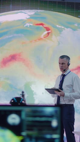 vertical shot of middle aged man with headset using tablet and talking to employees while researching global warming problem in office