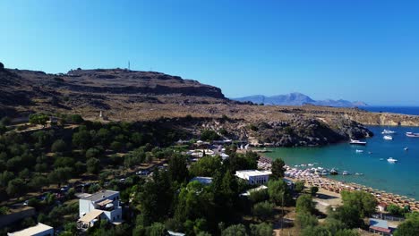 Lindos-beach-and-village-in-Rhodes,-Greece-with-Acropolis-of-Lindos,-houses-and-Mediterranean-sea-during-the-day-filmed-with-the-drone