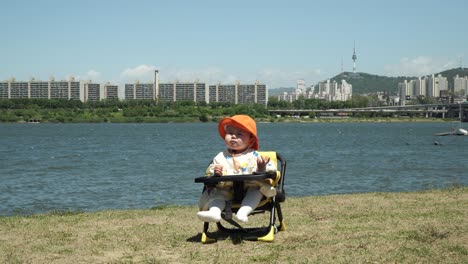 adorable one-year-old toddler in outdoor baby seat under the sunlight by the riverbank in seoul, south korea