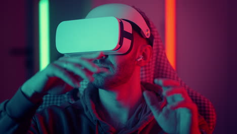 cyber gamer in vr glasses plays virtual reality game in neon futuristic space. gaming concept. young handsome man looks around and shooting from virtual blaster gun. high quality 4k footage