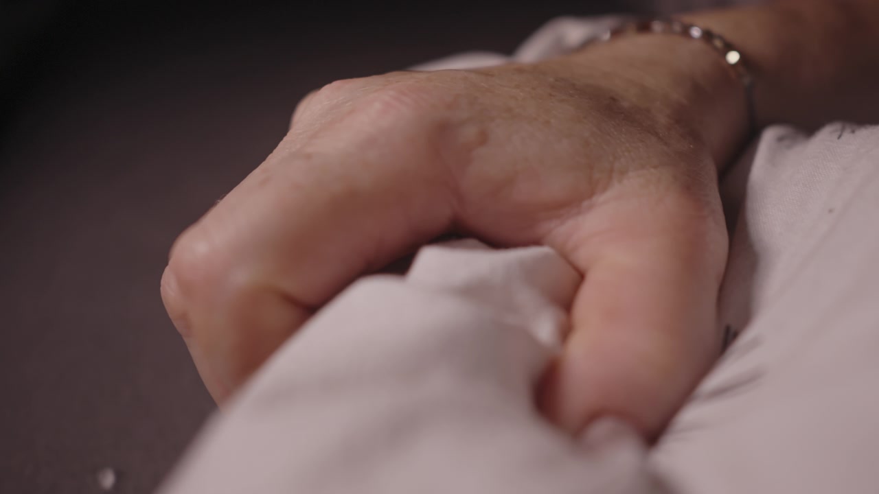 Primer plano de una mano sujetando suavemente una sábana blanca, transmitiendo intimidad, comodidad, vulnerabilidad y conexión emocional. Adecuado para bienestar, romance y narración cinematográfica