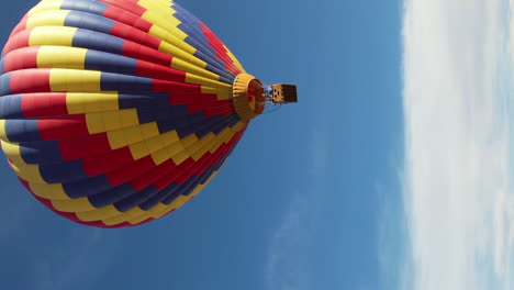 Vista-Aérea-Vertical-De-Coloridos-Globos-Aerostáticos-Volando-Bajo-El-Cielo-Azul-En-Un-Día-Soleado,-Disparo-De-Drones