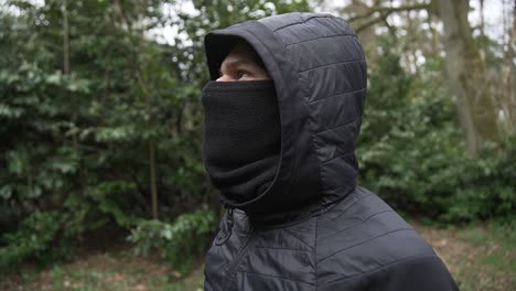 joven matón hispano con máscara y gorra en chaqueta negra de pie en el puesto de observación