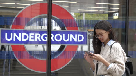 elegante joven mujer profesional esperando fuera de la estación de metro de londres usando su teléfono inteligente