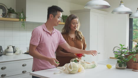 asian couple unpack fresh and healthy local food in zero waste packaging from bag in kitchen at home