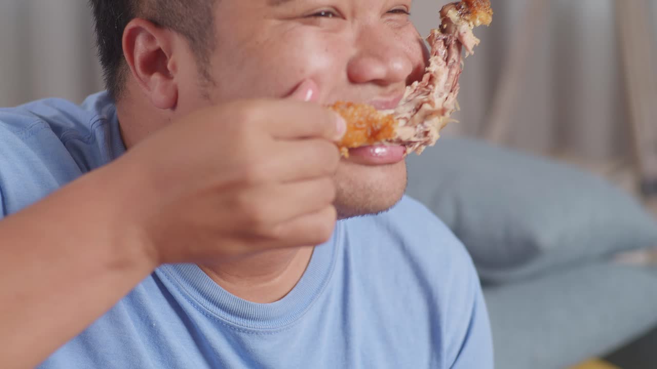 Close Up Of A Fat Asian Man Eating Fast Food Having Fried Chicken On A Sofa In The Living Room At Home