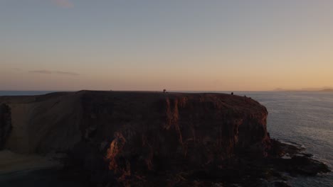 group of tourists standing on a cliff at papagayo beach, facing the ocean as the sun sets