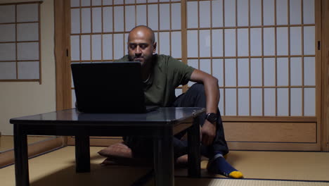 en un interior japonés tradicional, un hombre integra sin problemas la tecnología moderna en el ambiente sereno, trabajando en su portátil abriendo la tapa