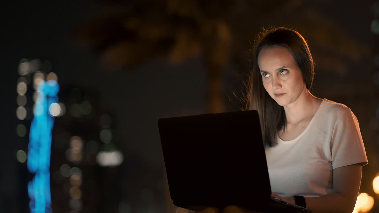 una mujer desarrolladora de software se sienta en un parque en una noche de verano en la ciudad y escribe código mirando la pantalla de una computadora portátil. imprime el artículo en una computadora portable. blogger responde a las publicaciones