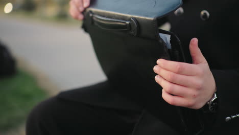 close up of individual in black clothing seated, searching through briefcase for document, background featuring unclear moving object with light effect